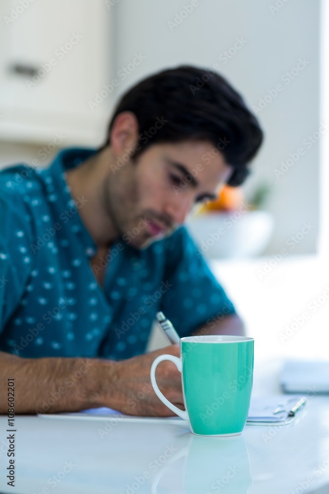 Man writing on clipboard with coffee mug on table Man writing on clipboard with coffee mug on table