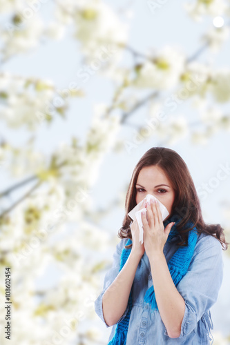 Junge Frau mit Taschentuch und Schnupfen vor Frühlingsblüten
