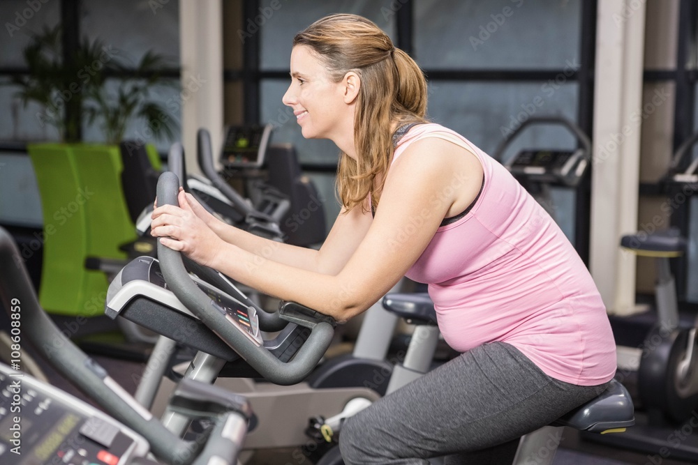 Smiling pregnant woman sitting on exercise bike Smiling pregnant woman sitting on exercise bike
