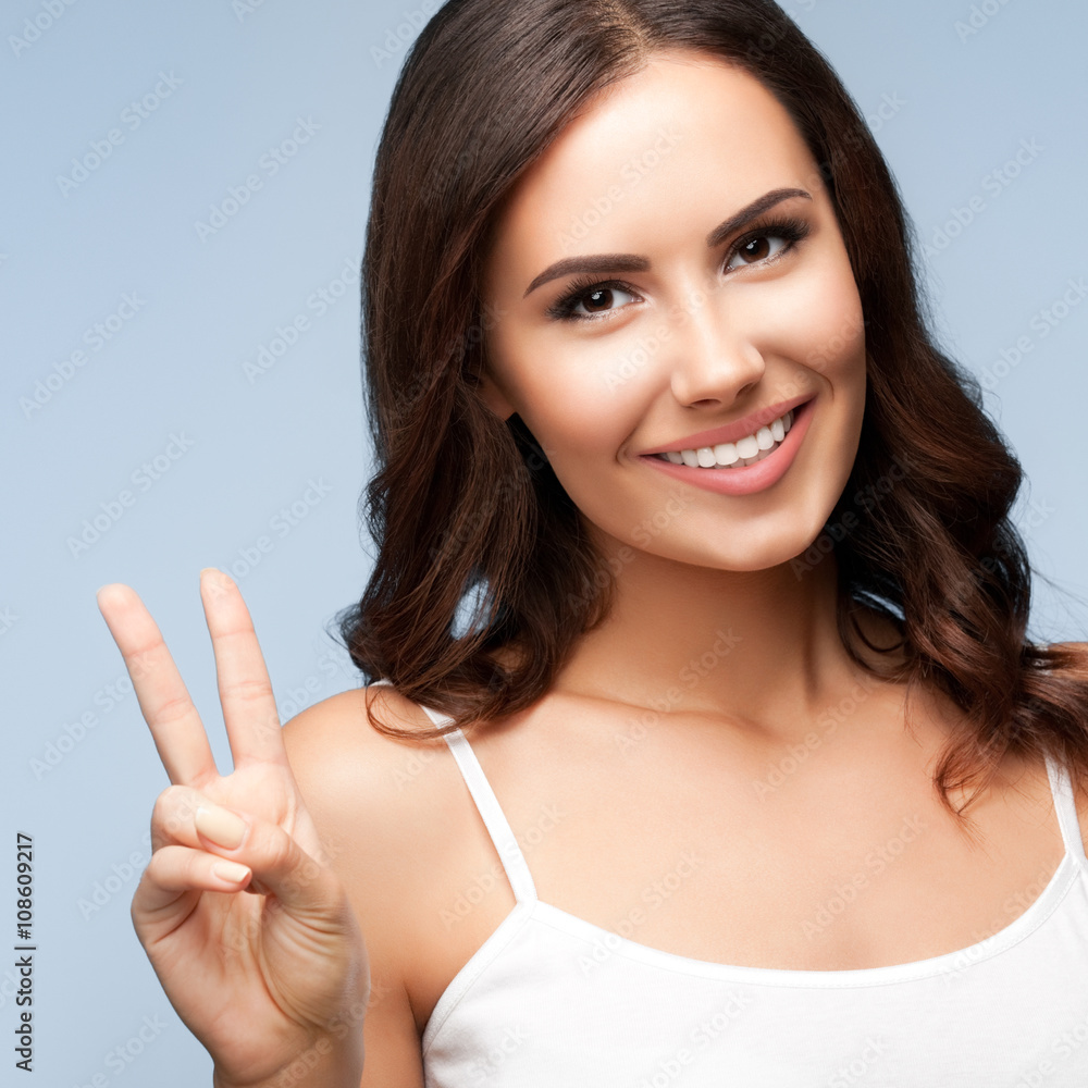 Woman showing two fingers or victory gesture, on grey Woman showing two fingers or victory gesture, on grey