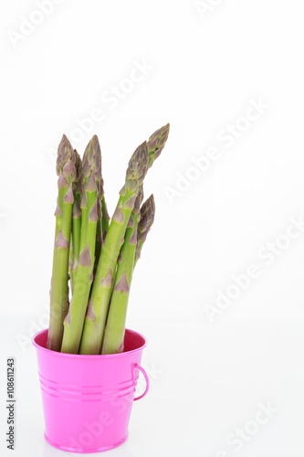 Asparagus spears in pink bucket, isolated on white background with copy-space