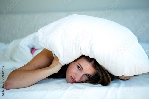 woman hiding in bed covering herself with a pillow