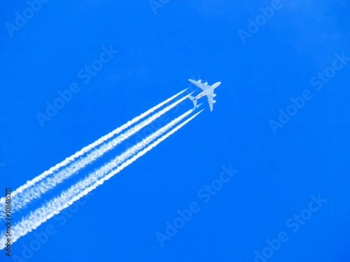 Airplane with chemtrails on blue sky photo