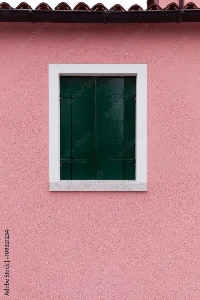 Window with dark green shutters on light pink wall