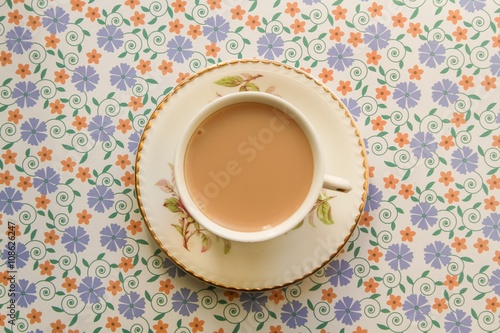 Cup of milky tea on a floral background 