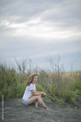 Wallpaper Mural loneliness. Girl with wavy hair on the beach with black sand in a light white top and denim varieties Torontodigital.ca