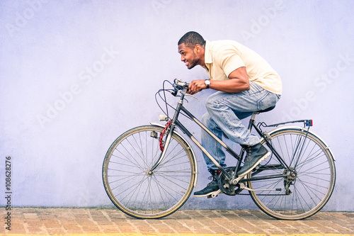 Black American African man in funny scene with locked old bike - Young afroamerican guy riding vintage bicycle with red padlock safe chained to wheel - Fun concept of cycle theft and security tools 