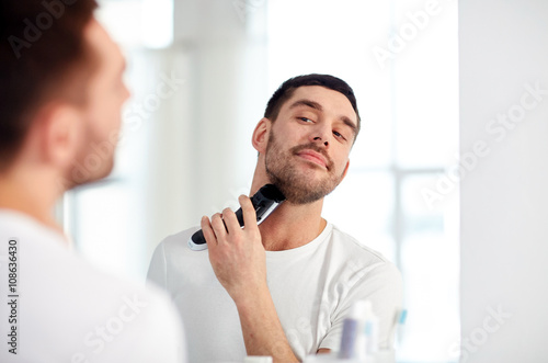 Photos man shaving beard with trimmer at bathroom