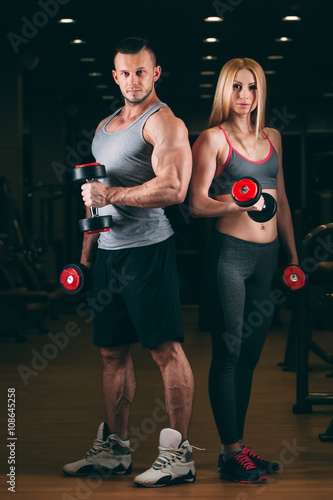 beautiful young sporty sexy couple showing muscle and workout in gym dumbbell