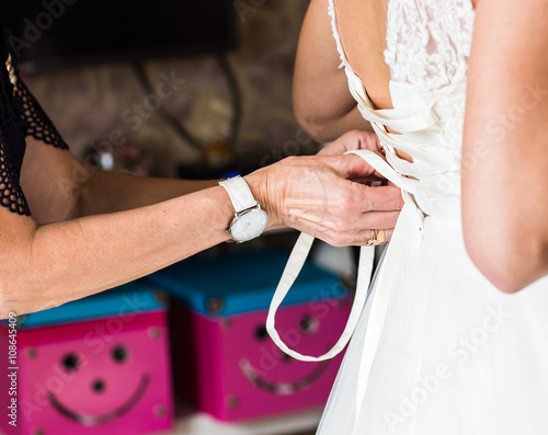 Bridesmaid is helping the bride to dress