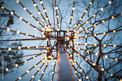 Fototapeta Naklejka Na Ścianę i Meble -  light bulbs on string wire hanging on poles against sunset sky