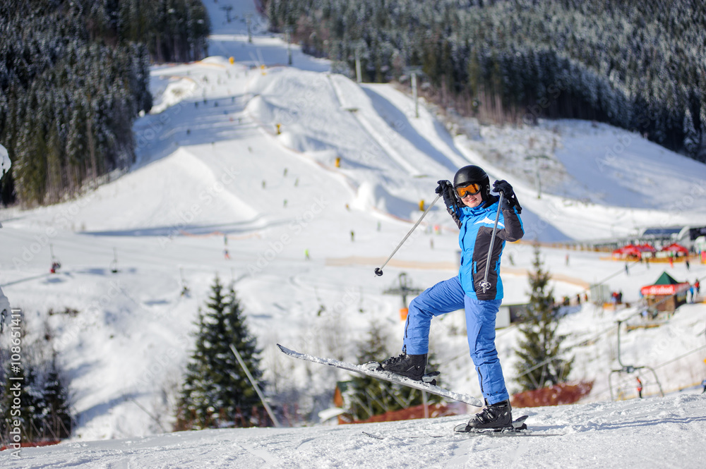 Full length Portrait of happy female skier against ski slopes and ski-lift on background. Woman is wearing helmet skiing glasses gloves and blue ski suit. Winter sports concept. Bukovel, Ukraine