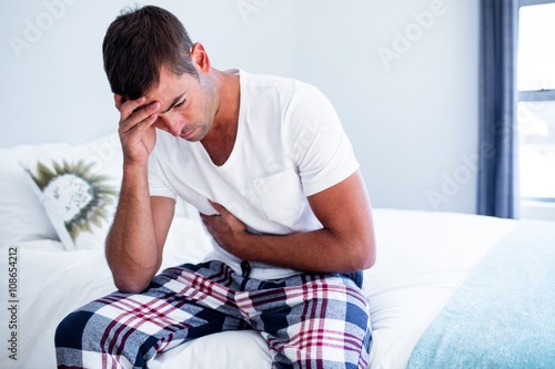 Cuadro en lienzo Young man sitting with stomach pain on bed