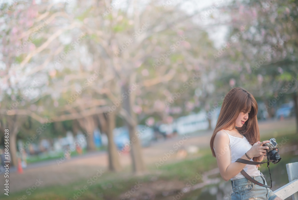 beautiful asian woman photographer holding camera seat Standing behind a tree with sunset time (selective focus)