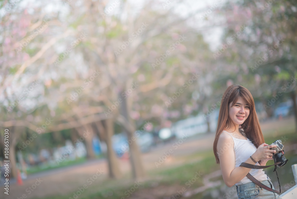 beautiful asian woman photographer holding camera seat Standing behind a tree with sunset time (selective focus) beautiful asian woman photographer holding camera seat Standing behind a tree with sunset time (selective focus)