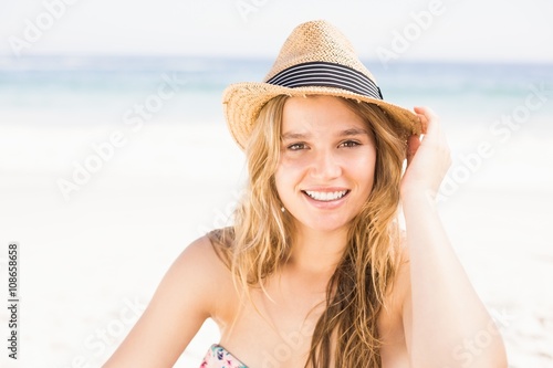 Portrait of pretty woman in bikini and hat sitting on the beach