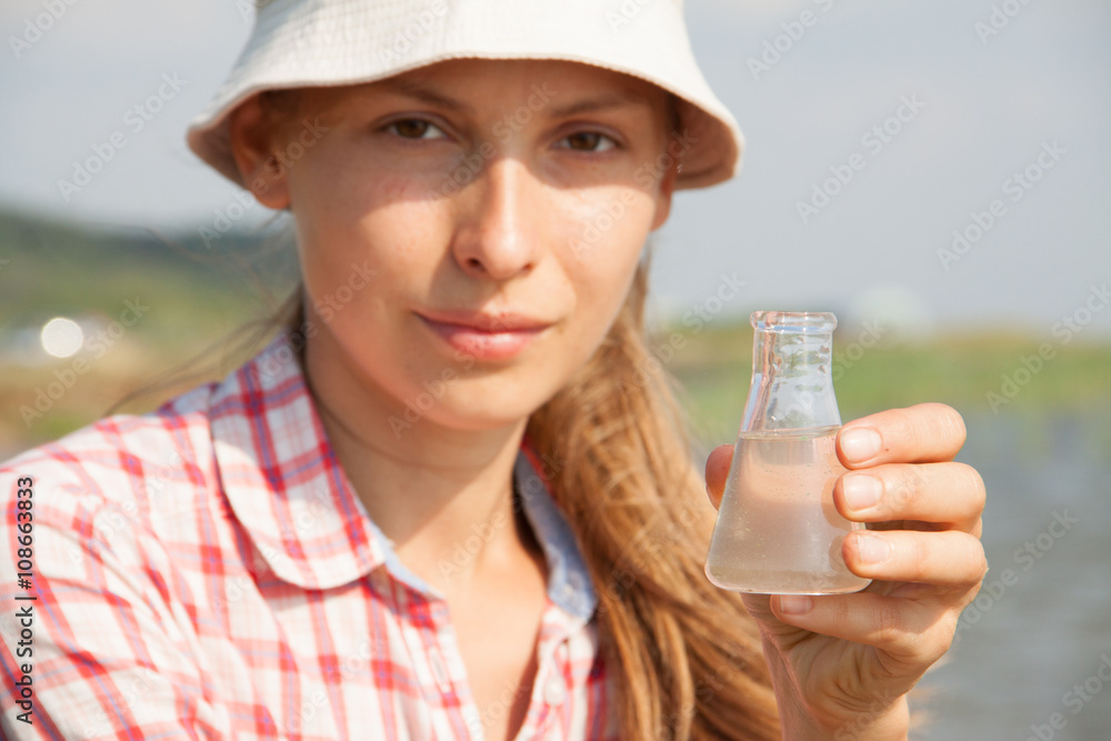 Water Purity Test. Woman holding a chemical flask with water, lake or river in the background. Water Purity Test. Woman holding a chemical flask with water, lake or river in the background.
