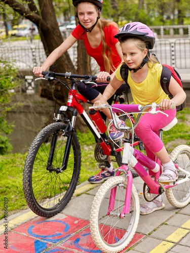 Bikes bicyclist girl. Girls wearing bicycle helmet  with rucksack ciclyng bicycle. Girls children cycling on yellow bike lane. Bike share program save money and time. Child in foreground  teenager on photo