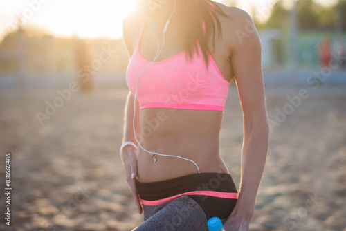 Beautiful fitness athlete woman resting drinking water after work out exercising on beach summer evening in sunny sunshine outdoor portrait