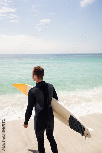 Rear view of surfer with surfboard standing on the beach