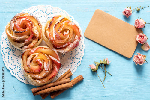 Homemade Apple rose cake with sugar powder on blue  wooden background.
Top view.  Handmade gift for mom/ Mothers day greeting card.

