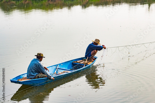 Fotografia, Obraz The fisherman in the boat use net to catch fish in the river.