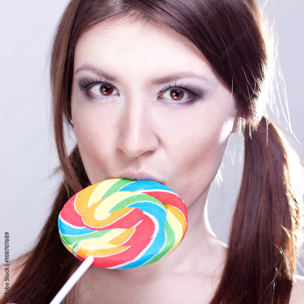 Beautiful girl with brown hair, glamorous make-up, fashion style portrait, holding candy in her hand sexy look