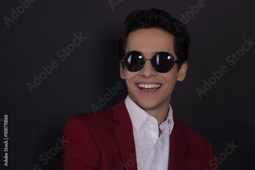 Portrait of a smille  young man in suit and glasses standing against black background © elenakibrik