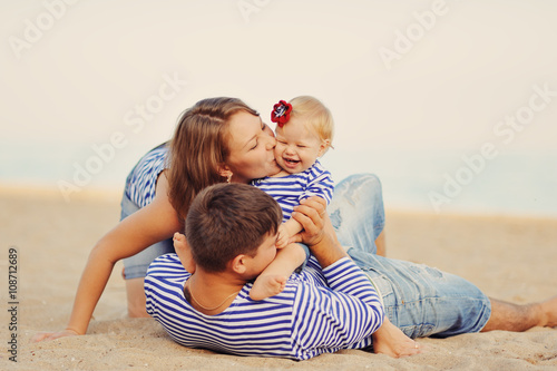 Папа, мама и маленькая дочь в полосатых майках играют на пляже