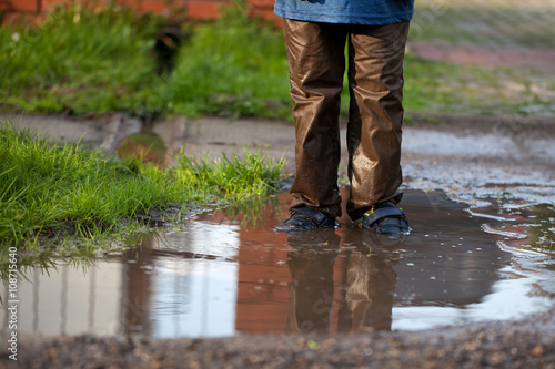 Little boy splashing in a mud puddle, jumping into a puddle 