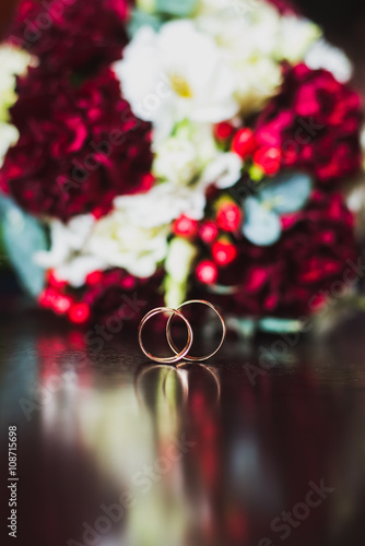 Wedding gold rings on a dark wooden table. A bouquet of flowers nearby.