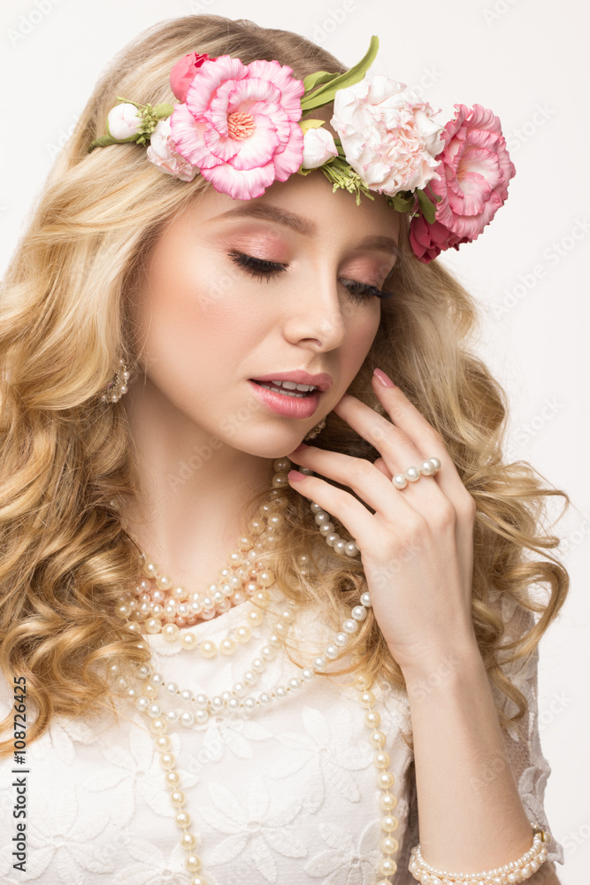 Close-up beauty portrait. Beautiful blonde girl with wreath of flowers. Touching pearl necklace. Looking down. Isolated on white background
