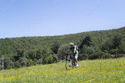 Cyclist man is biking in a green field on a spring day