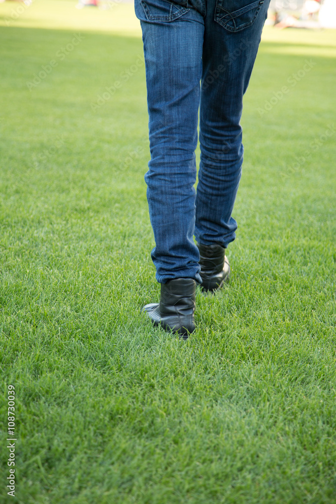 Leg of a man with Blue Jeans and Black Shoes is walking on the Meadow Leg of a man with Blue Jeans and Black Shoes is walking on the Meadow