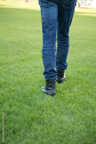 Leg of a man with Blue Jeans and Black Shoes is walking on the Meadow