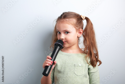 Cute fun kid girl singing song in microphone on blue background.