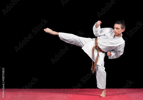 Karate boy in white kimono fighting isolated on black background