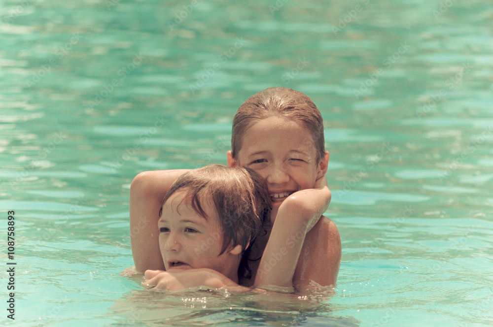 Two happy boys wrestling in the swimming pool.