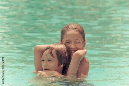 Two happy boys wrestling in the swimming pool.