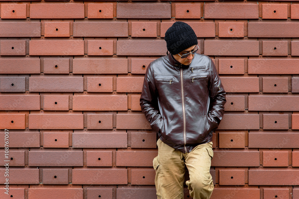 An Asian Man in a Brown Jacket Leans Against the Wall