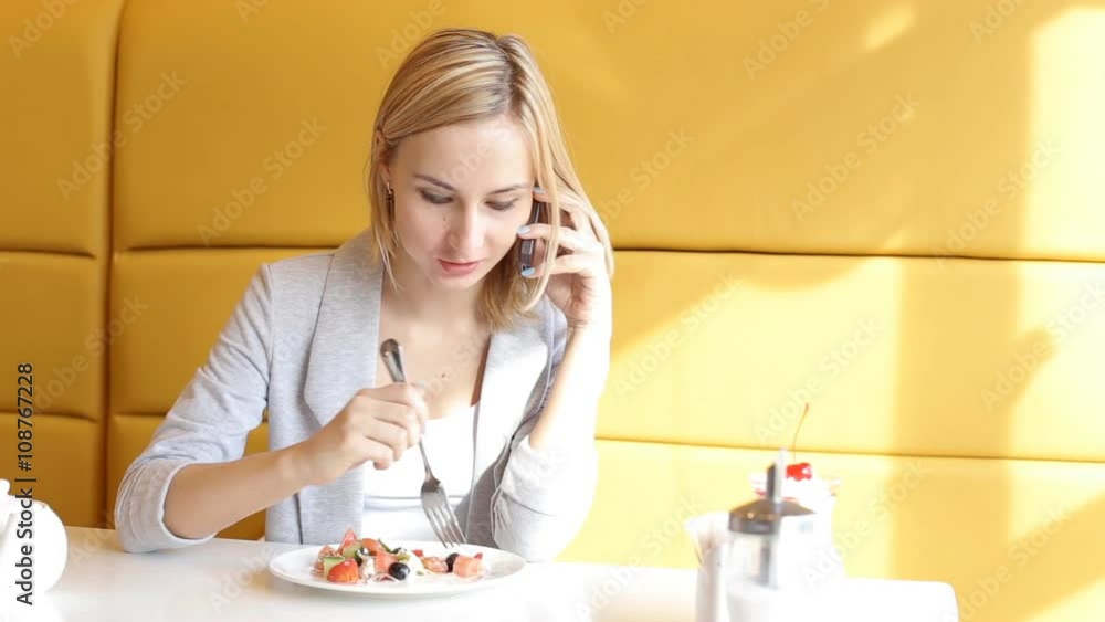 Young, pretty woman talking on cellphone, eating salad in cafe Young, pretty woman talking on cellphone, eating salad in cafe