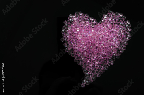 Pink crystals arranged in a heart shape on a black background
