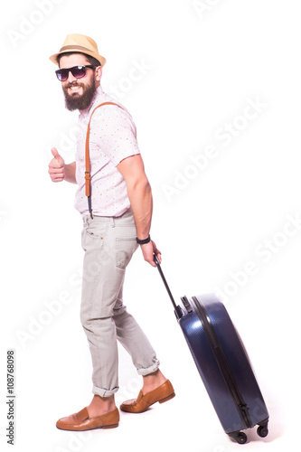 Young creative tourist man is posing with suitcase on grey background.