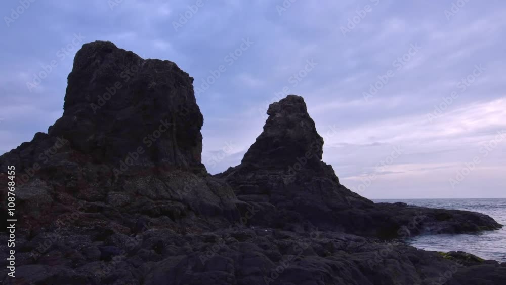Timelapse outdoors on beautiful rocky coast as gray clouds drift by two towering rocks over ocean surf Timelapse outdoors on beautiful rocky coast as gray clouds drift by two towering rocks over ocean surf