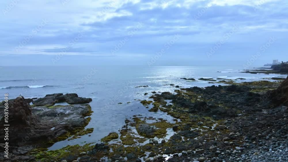 Time lapse outdoors on beautiful rocky coast as gray clouds drift over calm surf in Rosarito, Baja California, Mexico Time lapse outdoors on beautiful rocky coast as gray clouds drift over calm surf in Rosarito, Baja California, Mexico