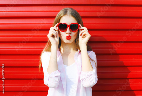 Pretty woman in red sunglasses blowing lips kiss over colorful b