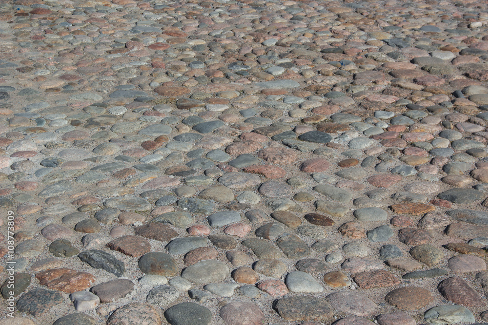 The ancient paving stones. The cobblestones of the ancient city. Natural surface roads. Background and texture of the stones. Round stones of the street. Close up The ancient paving stones. The cobblestones of the ancient city. Natural surface roads. Background and texture of the stones. Round stones of the street. Close up