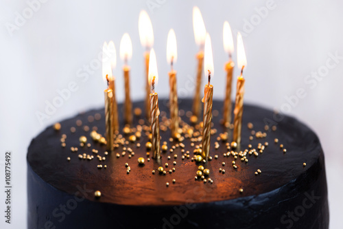 Canvas Print Black round birthday cake with burning golden candles on white b