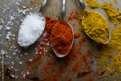 salt, paprika and curry on steel spoons