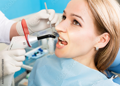 The reception was at the female dentist. Doctor examines the oral cavity on tooth decay. Caries protection. Tooth decay treatment. Dentist working with dental polymerization lamp in oral cavity